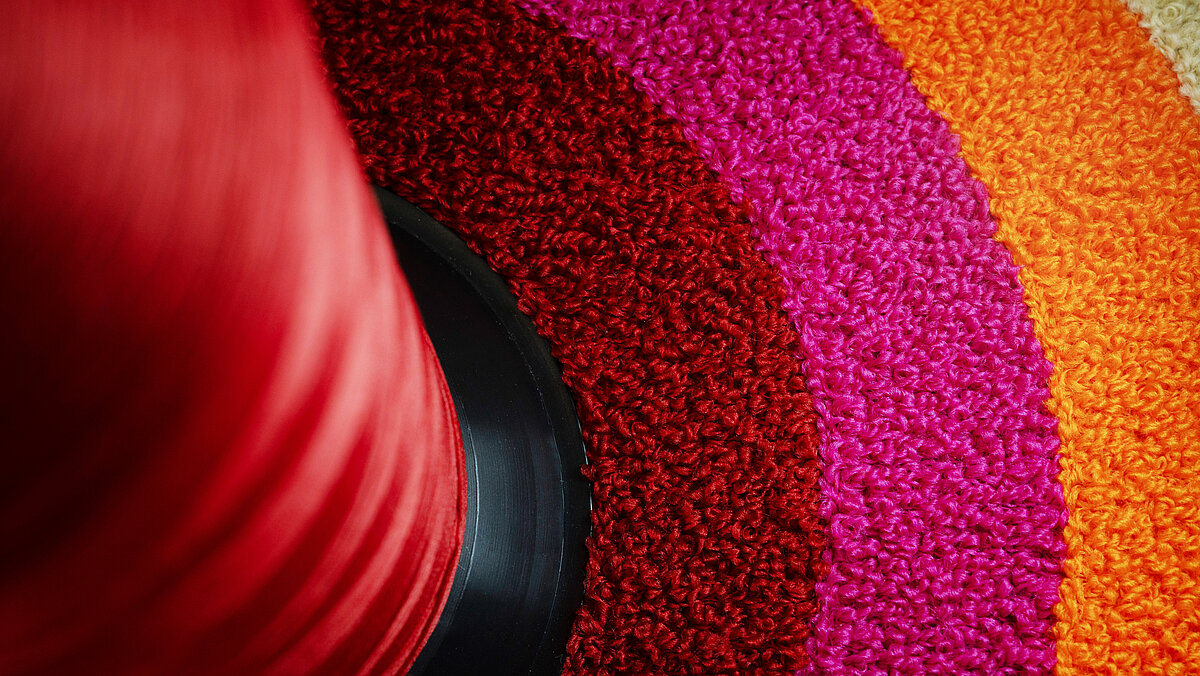 Red chenille thread cone placed within a colourful chenille embroidered circle in red, pink and orange shades.