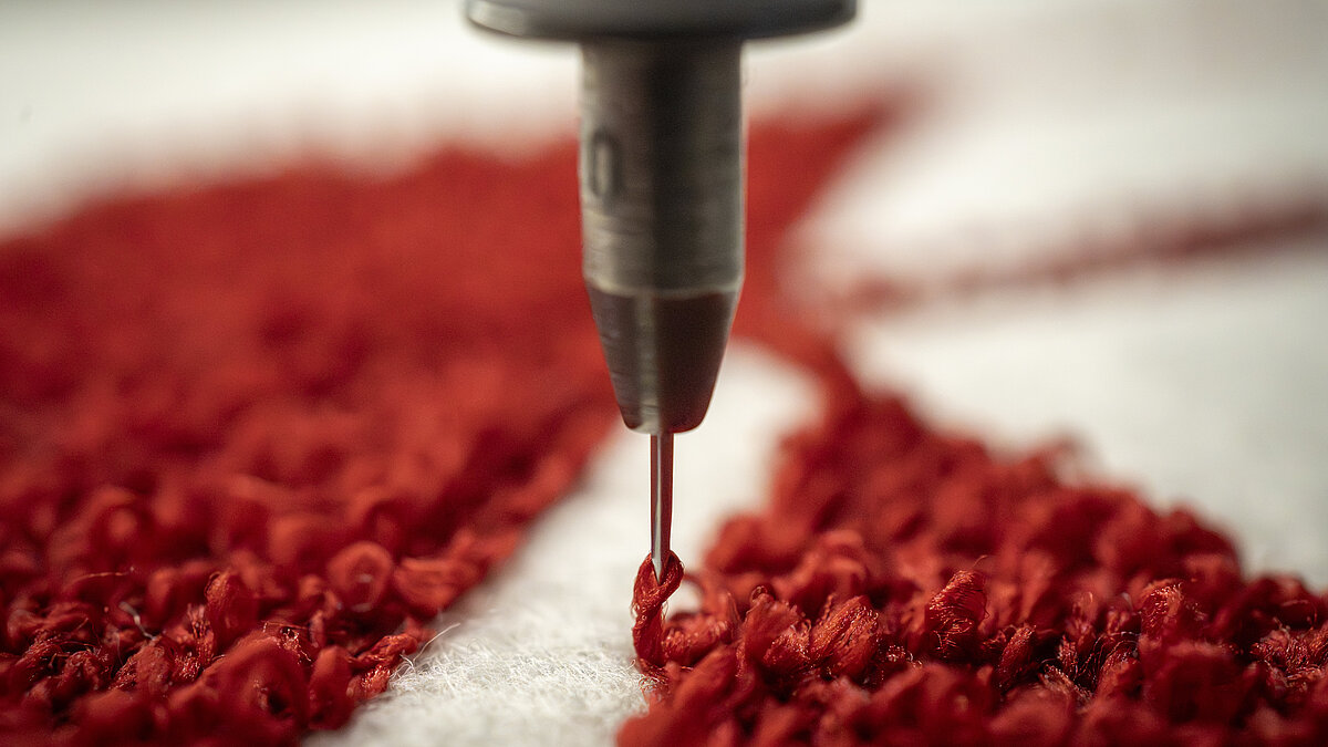 Close-up of red chenille embroidery on white fabric, showing the special chenille needle forming the characteristic looped stitch.